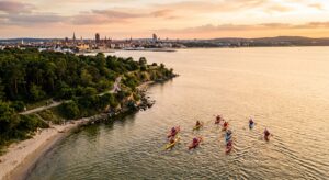 A professional, high-angle editorial shot of a group of kayakers paddling along the scenic, calm coa